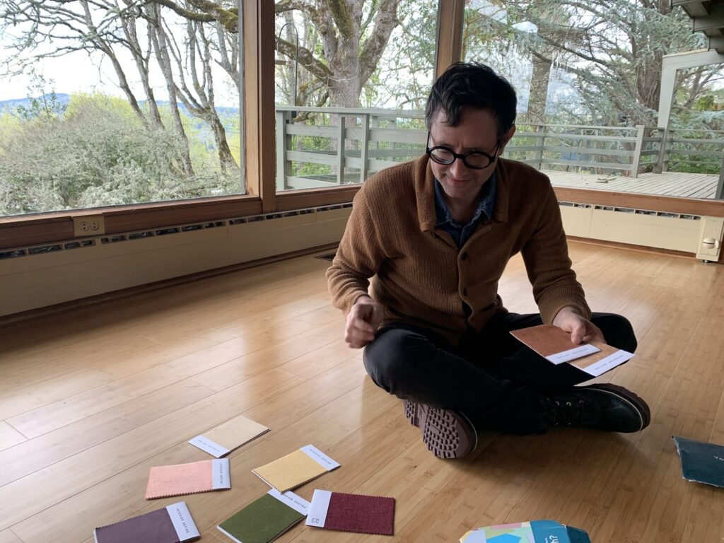 A man in glasses sits on floor surrounded by upholstery samples
